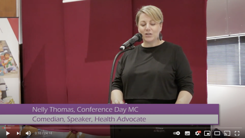 Video screenshot showing a professional looking woman speaking into a microphone