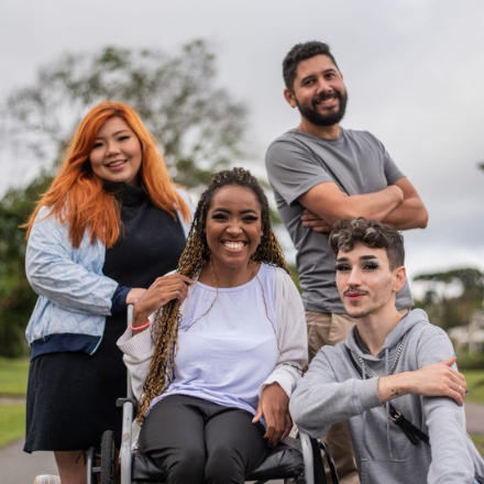 Diversity group of people. A Japanese woman, a non-binary person, a Latino, and a black woman in a wheelchair.